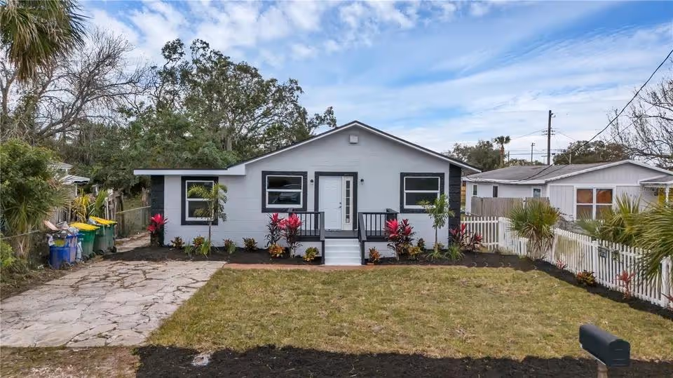 Single-story house with white exterior and black trim, a small front porch with stairs, landscaped front yard with grass and colorful plants.